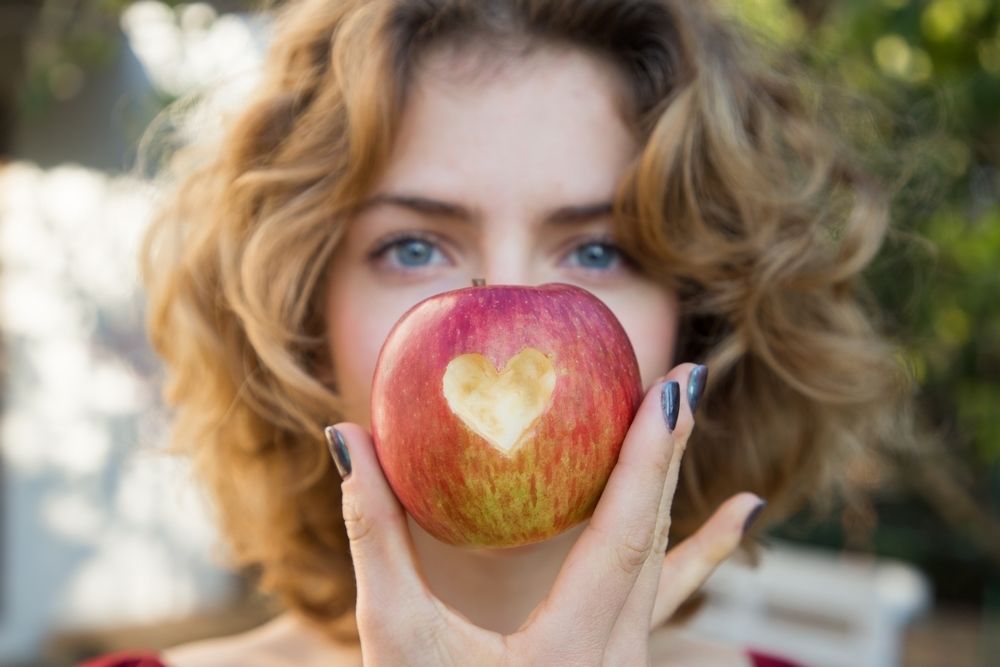 healthy eating - young woman holds a red apple in front of her face with a heart cut out in it. selective focus. proper vitamin nutrition. love concept. health care, cardiology