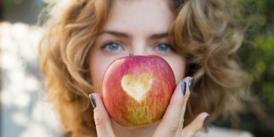 healthy eating - young woman holds a red apple in front of her face with a heart cut out in it. selective focus. proper vitamin nutrition. love concept. health care, cardiology